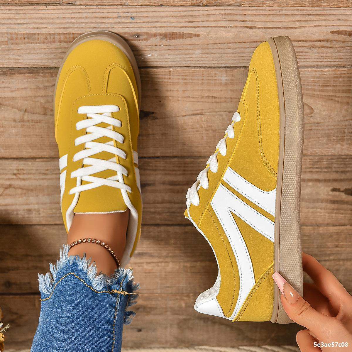 Yellow lace-up round toe flats shoes with white accents on wooden floor background