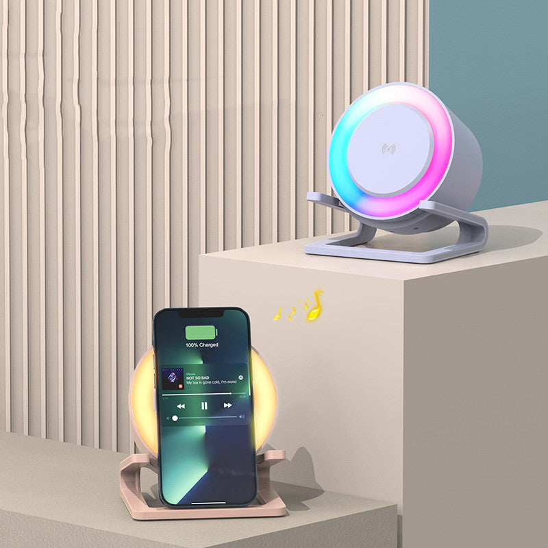 White Bluetooth speaker with wireless charging and colorful LED light ring next to a smartphone playing music and charging wirelessly