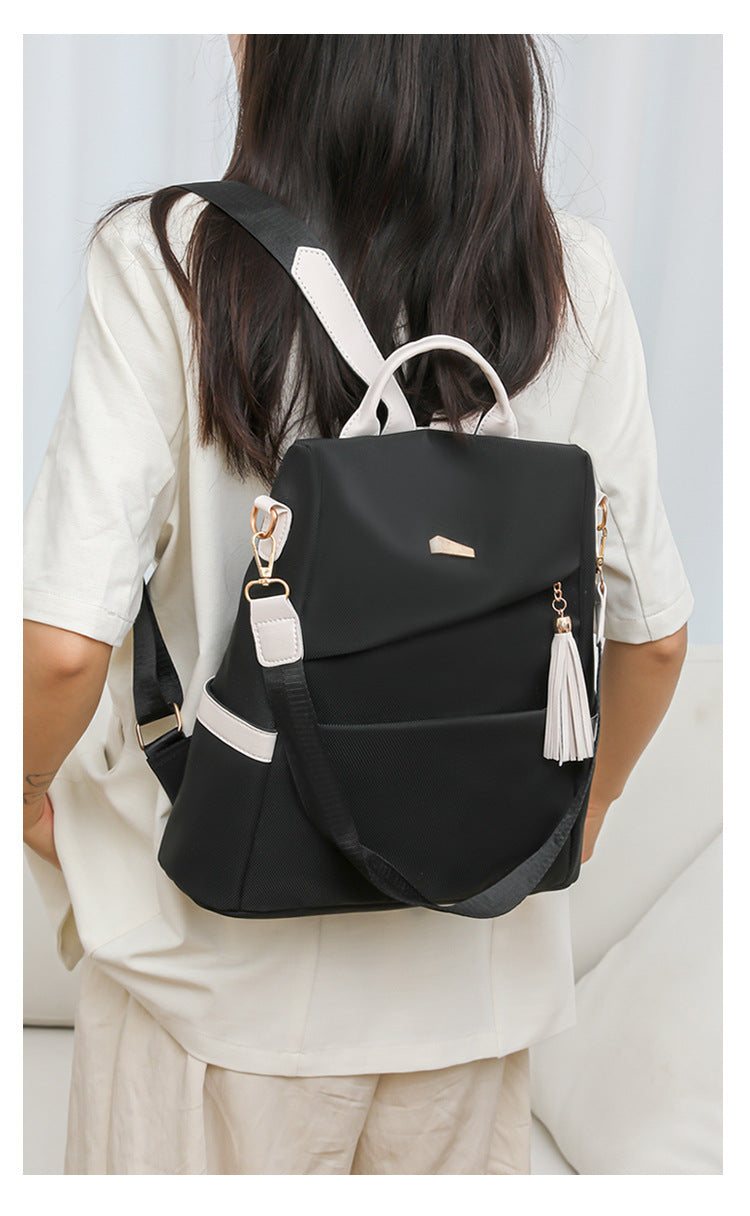 Oxford cloth stitching women’s black anti-theft backpack with white accents and tassel, worn by a woman